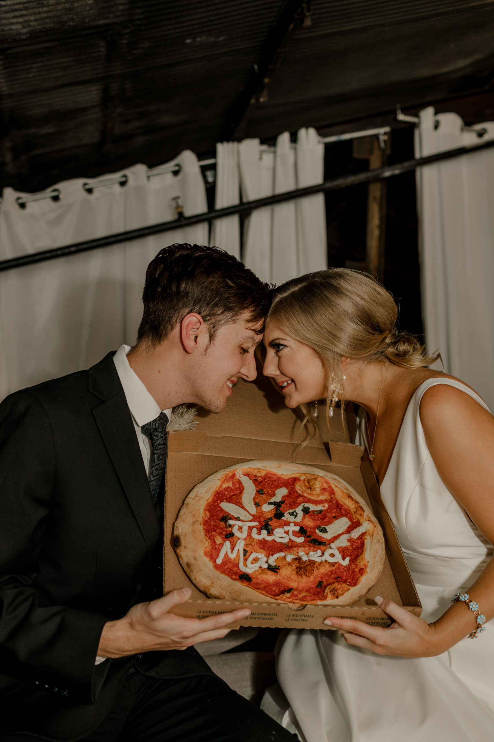 bride and groom facing each other with a just married pizza